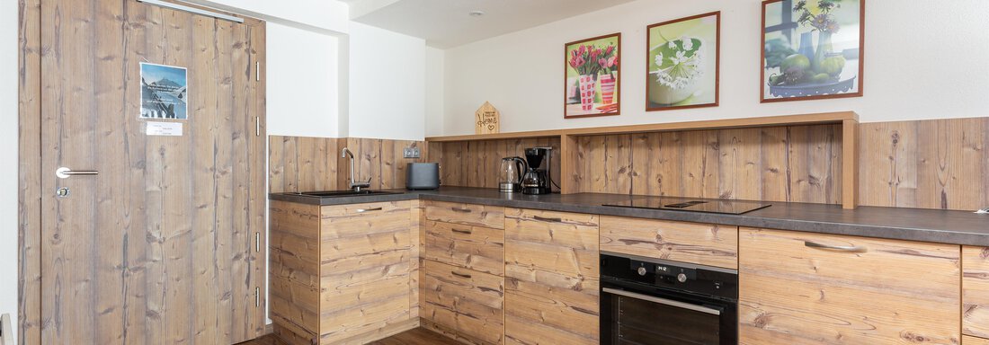 A modern kitchen with wooden furniture and a cozy atmosphere. The walls are decorated with pictures and the floor is made of high-quality wood. - Garni Stefani - Vent