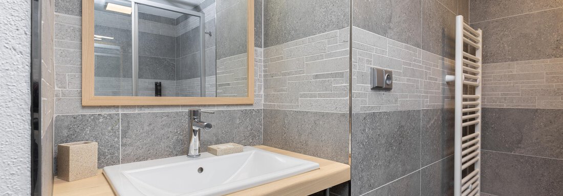 A modern bathroom with gray tiles and a large mirror. The sink area is clearly structured and features a towel warmer. - Garni Stefani - Vent