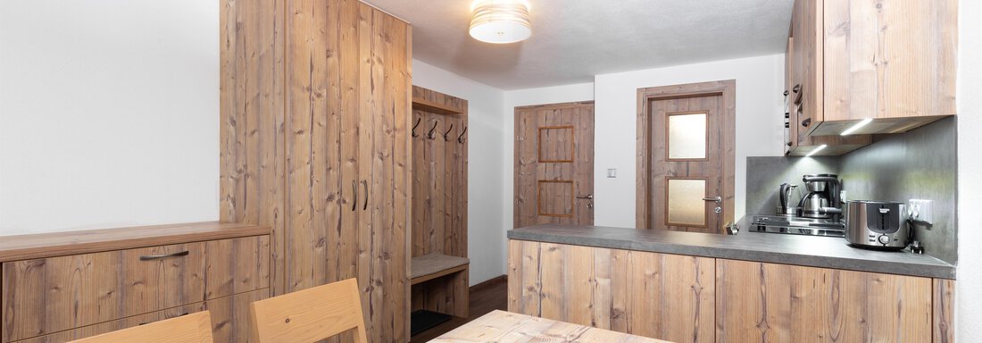 A modern kitchen made of wood with a dining table and chairs. The walls and furniture are in warm wooden tones. - Garni Stefani - Vent