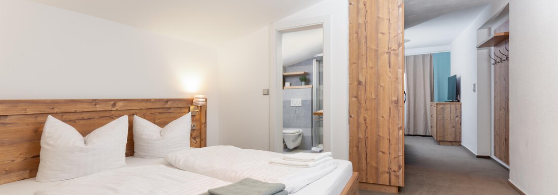 A cozy hotel room with a large double bed and bright walls. The room is modernly furnished and offers a view of an adjacent area. - Garni Stefani - Vent