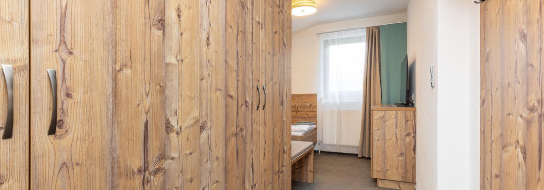A cozy room with wooden cabinets and a single bed. The window lets in plenty of daylight and creates a bright atmosphere. - Garni Stefani - Vent