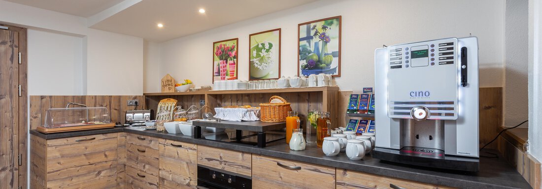 A modern kitchen with wooden furniture and a cooking area. Various kitchen appliances and food are on the countertop. - Garni Stefani - Vent