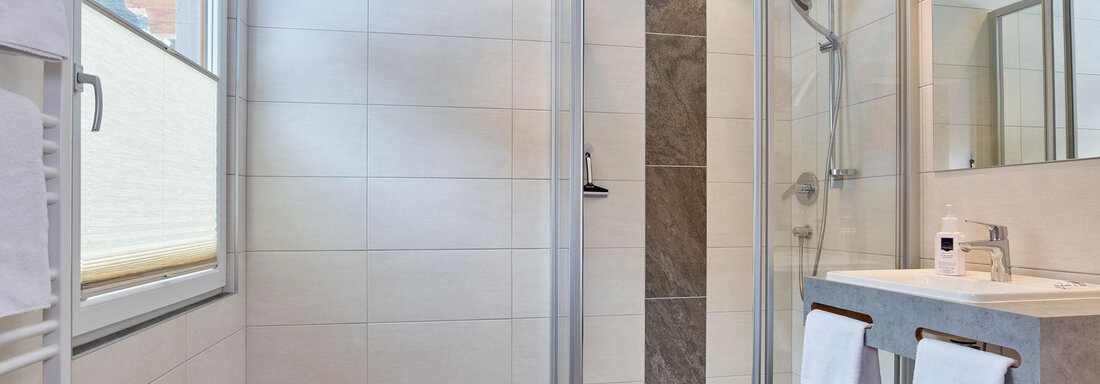 Ein modernes Badezimmer mit einer gläsernen Duschkabine und einem eleganten Waschbecken. Helle Fliesen und großzügige Fenster sorgen für ein freundliches Ambiente. - Hotel Vent - Vent