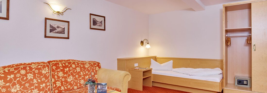 Ein gemütliches Zimmer mit einem roten Teppich und einem Sofa. Es gibt einen Tisch, einen Kleiderschrank und ein Einzelbett. - Hotel Vent - Vent