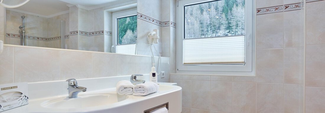 Ein modernes Badezimmer mit einer weißen Waschbecken und einem großen Spiegel. Der Boden ist mit rot-weißem Fliesenmuster gestaltet, und es gibt ein Fenster mit Blick ins Freie. - Hotel Vent - Vent