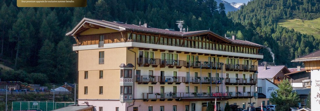Ein Hotelgebäude in den Bergen mit mehreren Fenstern und Balkonen. Im Vordergrund sind Fahrzeuge geparkt, und die Umgebung ist von grünen Hügeln umgeben. - Hotel Vent - Vent