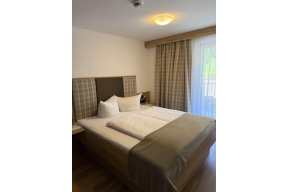 A cozy bedroom with a large bed and decorative pillows. The windows are adorned with light curtains that let in plenty of light. - Mein Weisskugel - Vent