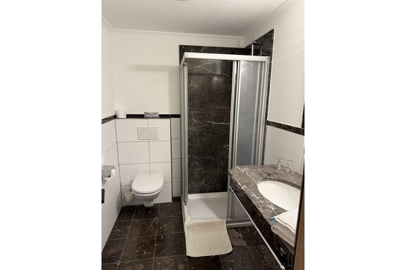 A modern bathroom with a shower and a marble sink. The walls are designed in a simple white and black style. - Mein Weisskugel - Vent