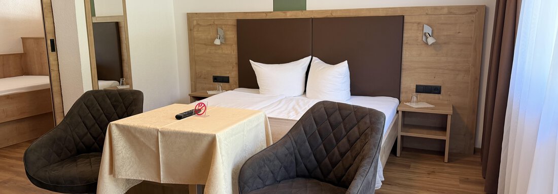 A modern room with a double bed, a small table, and two cozy chairs. Bright colors and natural materials give the space an inviting atmosphere. - Mein Weisskugel - Vent