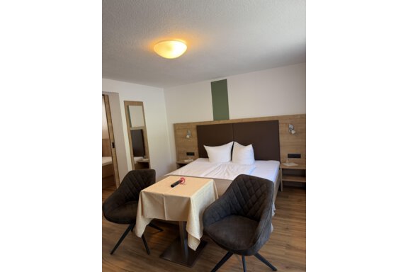 A modern hotel room with a double bed and two comfortable chairs. The table is set for guests, and there is a large mirror on the wall. - Mein Weisskugel - Vent