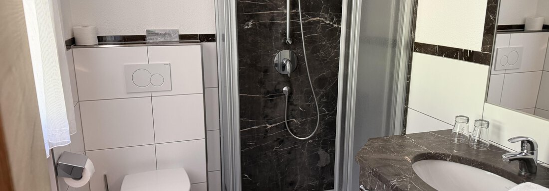 A modern bathroom with a shower and a sink. There are black tiles and a light-colored decor visible. - Mein Weisskugel - Vent