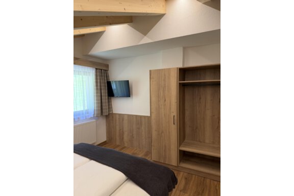 A modern bedroom with wood paneling and a flat-screen TV on the wall. The window is covered with a curtain and the room feels bright and inviting. - Mein Weisskugel - Vent