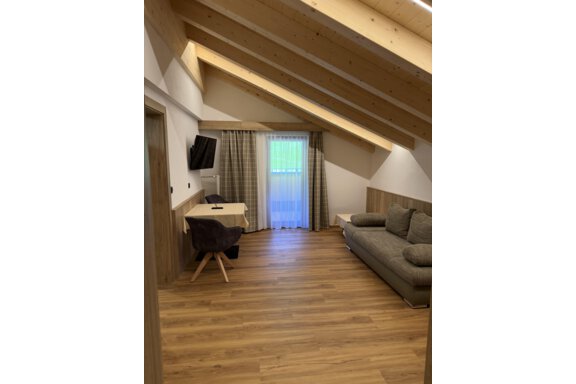 A cozy room with wooden ceilings and large windows. The furnishings include a sofa and a desk. - Mein Weisskugel - Vent
