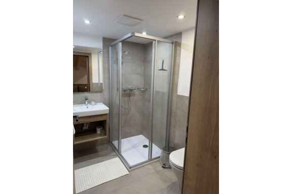 The image shows a modern bathroom with a glass shower and a stylish sink. The walls are in neutral colors and there is bright lighting. - Mein Weisskugel - Vent