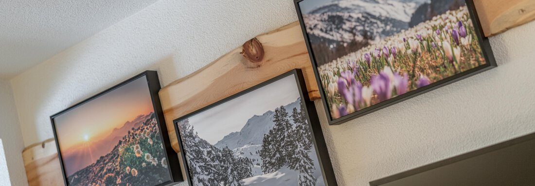 Three framed pictures hang on a wall that show different landscapes. The pictures include a sunset, snowy mountains, and blooming fields. - Garni Ötztal ROOMS & APARTS - Zwieselstein