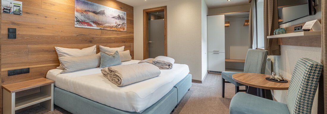 Bergzeit Duo | © Brunner Johannes, Michaela Jörg (CC C) A modern hotel room with a double bed and a wooden design. There is a small table, two chairs, and a television. - Garni Ötztal ROOMS & APARTS - Zwieselstein