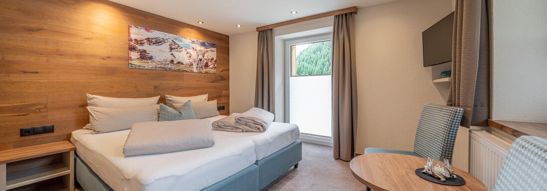 A modern room with a double bed and bright, cozy furnishings. The room features windows with a view and a sitting area. - Garni Ötztal ROOMS & APARTS - Zwieselstein