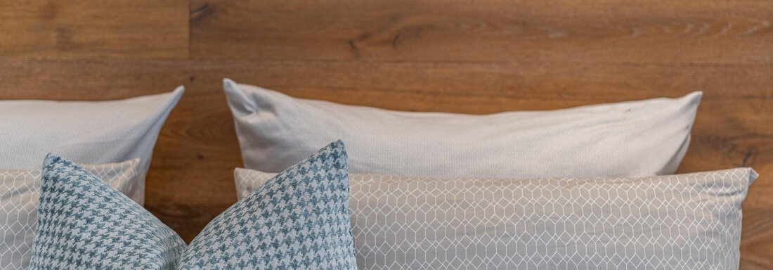 A cozy headboard with several cushions in soft colors. In the background, you can see wood paneling. - Garni Ötztal ROOMS & APARTS - Zwieselstein
