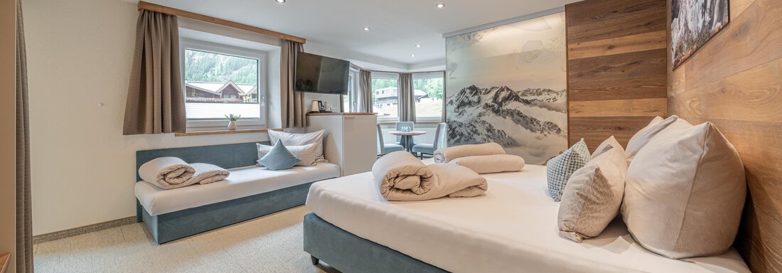 A modern room with two beds, pillows, and blankets. Large windows provide plenty of daylight and a cozy atmosphere. - Garni Ötztal ROOMS & APARTS - Zwieselstein