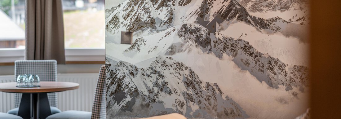 A modernly furnished room with a view of an impressive mountain landscape. The walls are decorated with a large-scale mountain motif. - Garni Ötztal ROOMS & APARTS - Zwieselstein