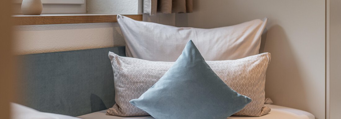A cozy sofa with several pillows in soft colors. Bright room with a window and decorative elements. - Garni Ötztal ROOMS & APARTS - Zwieselstein