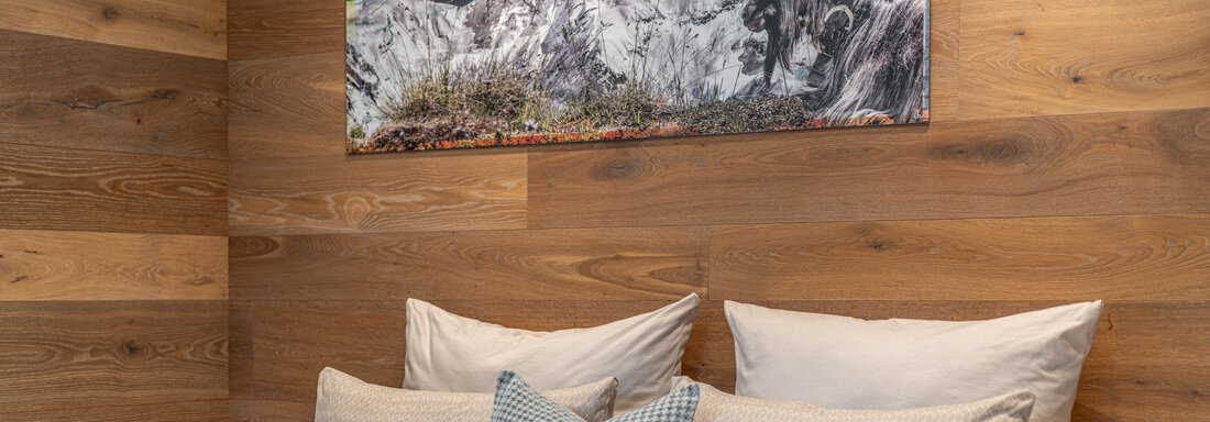 A cozy bedroom with wood paneling and large pillows. On the wall hangs a picture of a mountain landscape. - Garni Ötztal ROOMS & APARTS - Zwieselstein