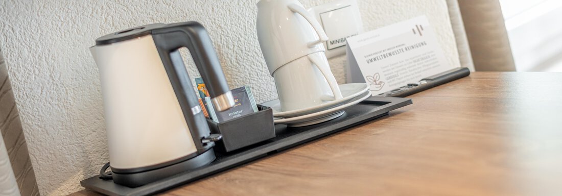 A kettle and a cup are on a wooden table. Next to it lies an information card. - Garni Ötztal ROOMS & APARTS - Zwieselstein
