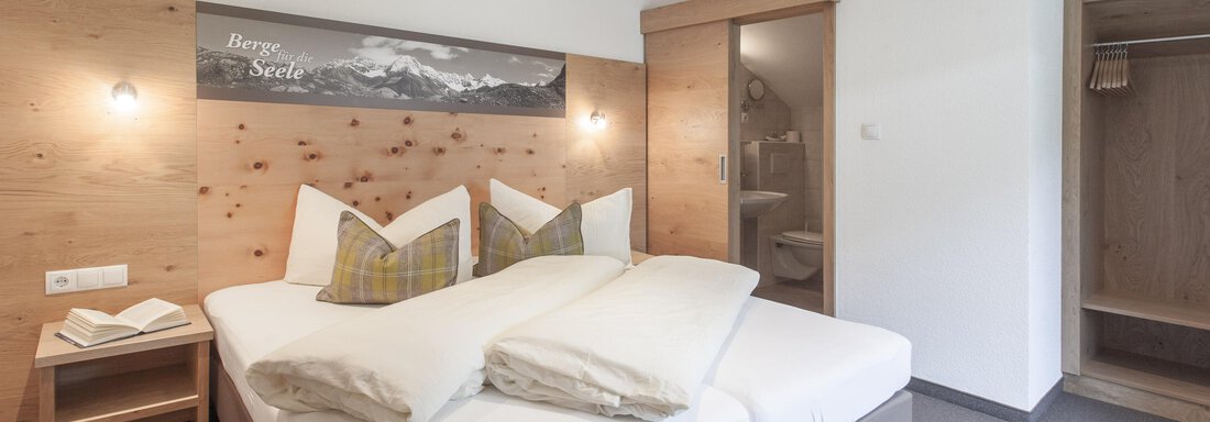 A modern bedroom with a double bed and a cozy decor. The wooden paneling and soft lighting create an inviting atmosphere. - Garni Ötztal ROOMS & APARTS - Zwieselstein