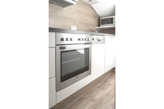 A modern kitchen with a stainless steel stove and white cabinets. The floor is made of light wood, and there is a microwave in the top right. - Garni Ötztal ROOMS & APARTS - Zwieselstein