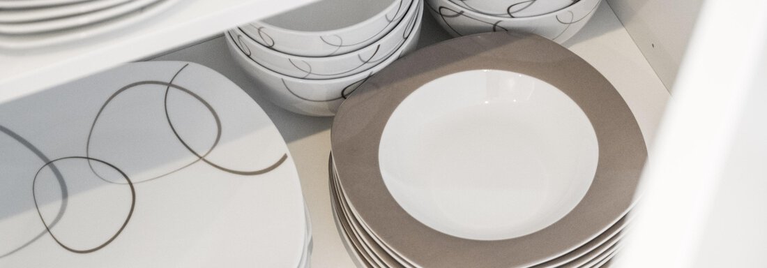 A treat of tableware in a cupboard. White plates with a modern design and decorative patterns are neatly stacked. - Garni Ötztal ROOMS & APARTS - Zwieselstein