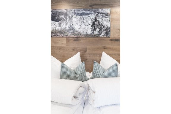 Ein gemütliches Schlafzimmer mit weißen Kissen und karierten Dekokissen. An der Wand hängt ein Bild von einer Berglandschaft. - Garni Ötztal ROOMS & APARTS - Zwieselstein