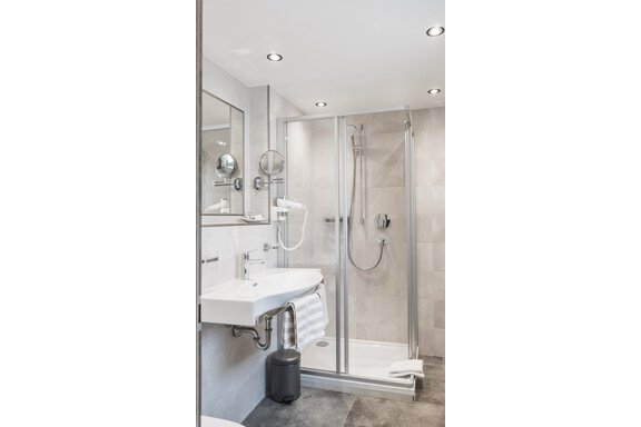 A modern bathroom with a shower and a sink. The walls are brightly tiled, and there is a large mirror wall. - Garni Ötztal ROOMS & APARTS - Zwieselstein