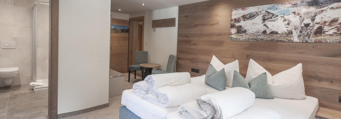 Ein modernes Schlafzimmer mit einem großen Bett und gemütlichen Kissen. Die Wände sind aus Holz, und es gibt ein Fenster, das natürliches Licht hereinlässt. - Garni Ötztal ROOMS & APARTS - Zwieselstein