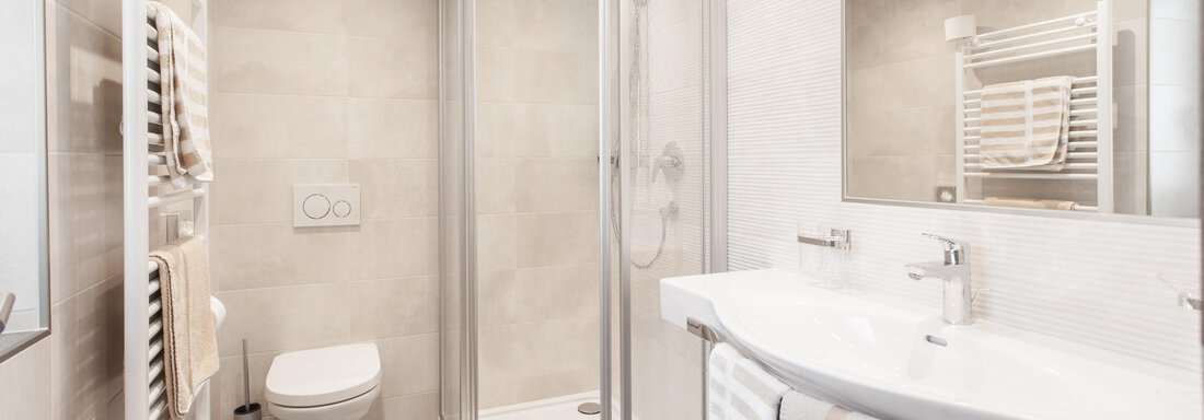 A modern bathroom with a shower and a sink. The walls are light and there is a towel radiator. - Garni Ötztal ROOMS & APARTS - Zwieselstein