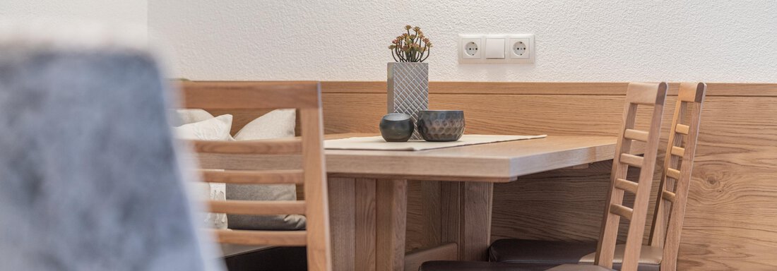 Ein gemütlicher Essbereich mit einem Holztisch und Stühlen. Der Tisch ist dekoriert mit Pflanzen und Kerzen, der Raum hat helle Wände und Holzdetails. - Garni Ötztal ROOMS & APARTS - Zwieselstein