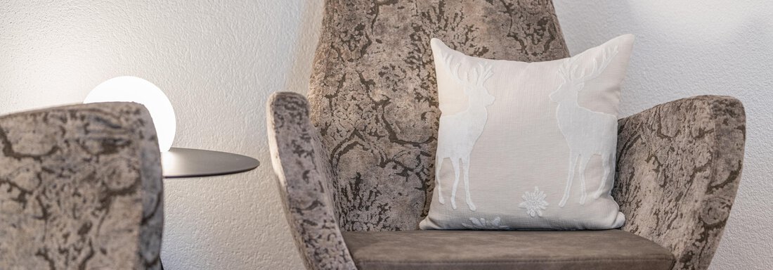 A cozy armchair with a decorative cushion. In the background, there is a modern lamp on a small table. - Garni Ötztal ROOMS & APARTS - Zwieselstein