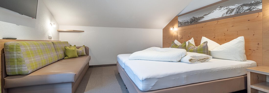 Ein gemütliches Schlafzimmer mit einem Doppelbett und einer bequemen Couch. Die Wände sind in neutralen Farben gehalten und schaffen eine entspannte Atmosphäre. - Garni Ötztal ROOMS & APARTS - Zwieselstein