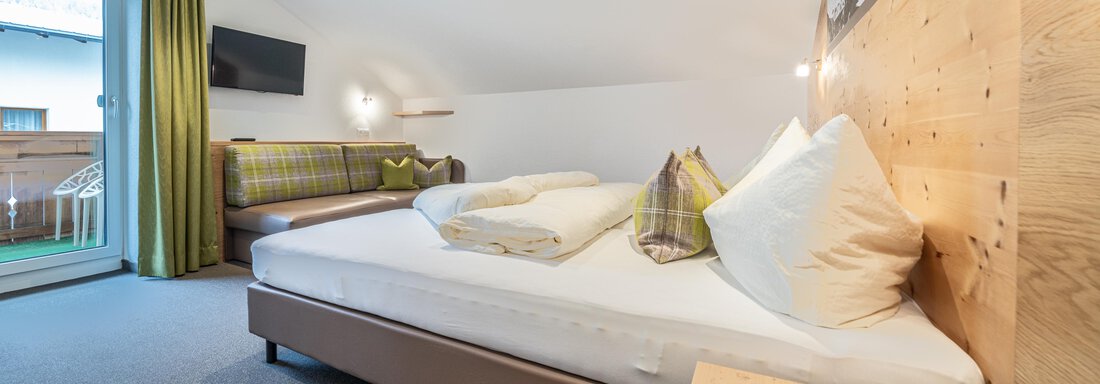 A cozy room with a large bed and bright pillows. The balcony offers a view and there is a seating area with a sofa. - Garni Ötztal ROOMS & APARTS - Zwieselstein