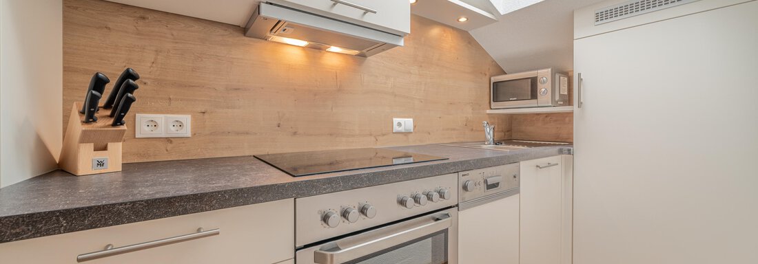 A modern kitchen with bright cabinets and wood details. It features a stove, a microwave, and a large window area. - Garni Ötztal ROOMS & APARTS - Zwieselstein