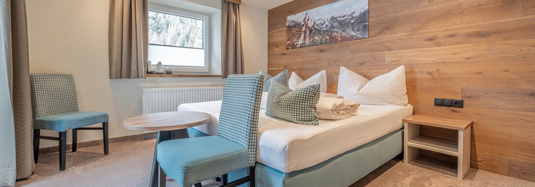 A cozy bedroom with a large bed and modern furniture. The warm wooden details create an inviting atmosphere. - Garni Ötztal ROOMS & APARTS - Zwieselstein
