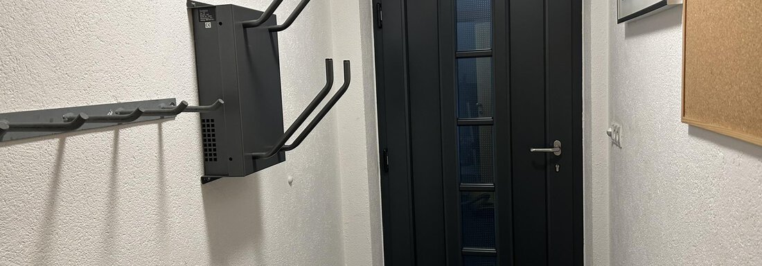 Ein schmaler Flur mit einer schwarzen Eingangstür und einem Garderobenhalter an der Wand. Rechts befindet sich ein Korkbrett für Notizen. - Haus Praxmarer - Zwieselstein