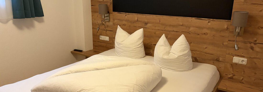 Ein gemütliches Schlafzimmer mit einem Doppelbett und holzverkleideter Wand. Die Bettwäsche ist sauber und ordentlich gefaltet, und es gibt zwei Nachttische mit Lampen. - Haus Praxmarer - Zwieselstein