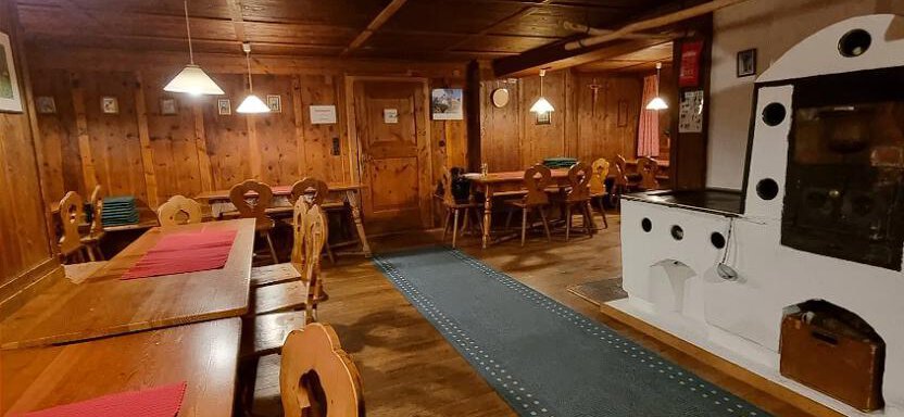 Ein gemütliches Restaurant mit Holzwänden und rustikalen Tischen. In der Mitte steht ein traditioneller Ofen, der für Wärme sorgt. - Talherberge Zwieselstein - Zwieselstein